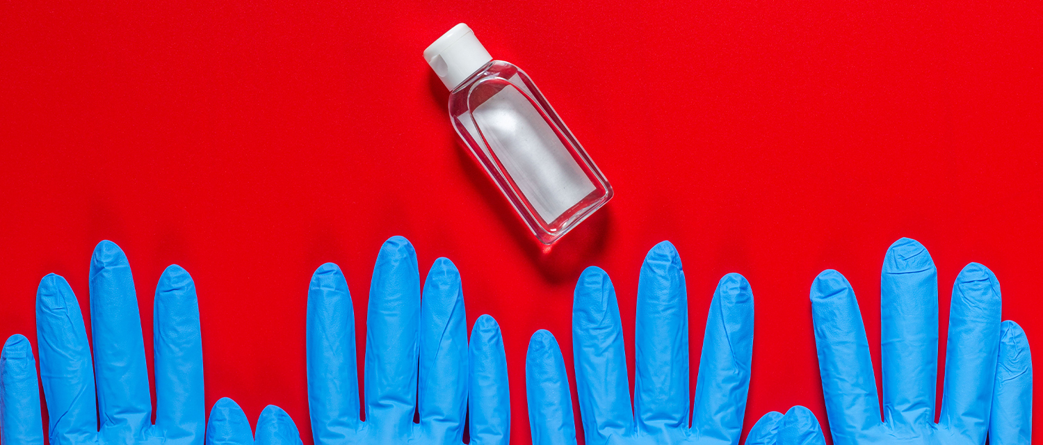 Desinfectante de manos y guantes de goma sobre fondo rojo.