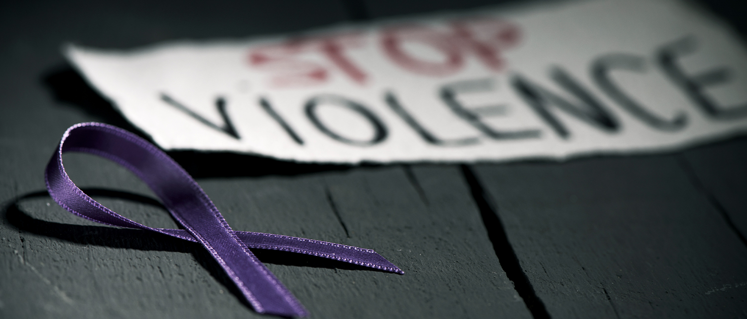 "Alto a la violencia" escrito en papel junto a una cinta violeta de concienciación sobre el abuso doméstico.